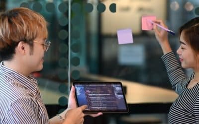 Dos colegas revisan resultados de pruebas de ERP en una tableta junto a notas adhesivas en un panel de vidrio